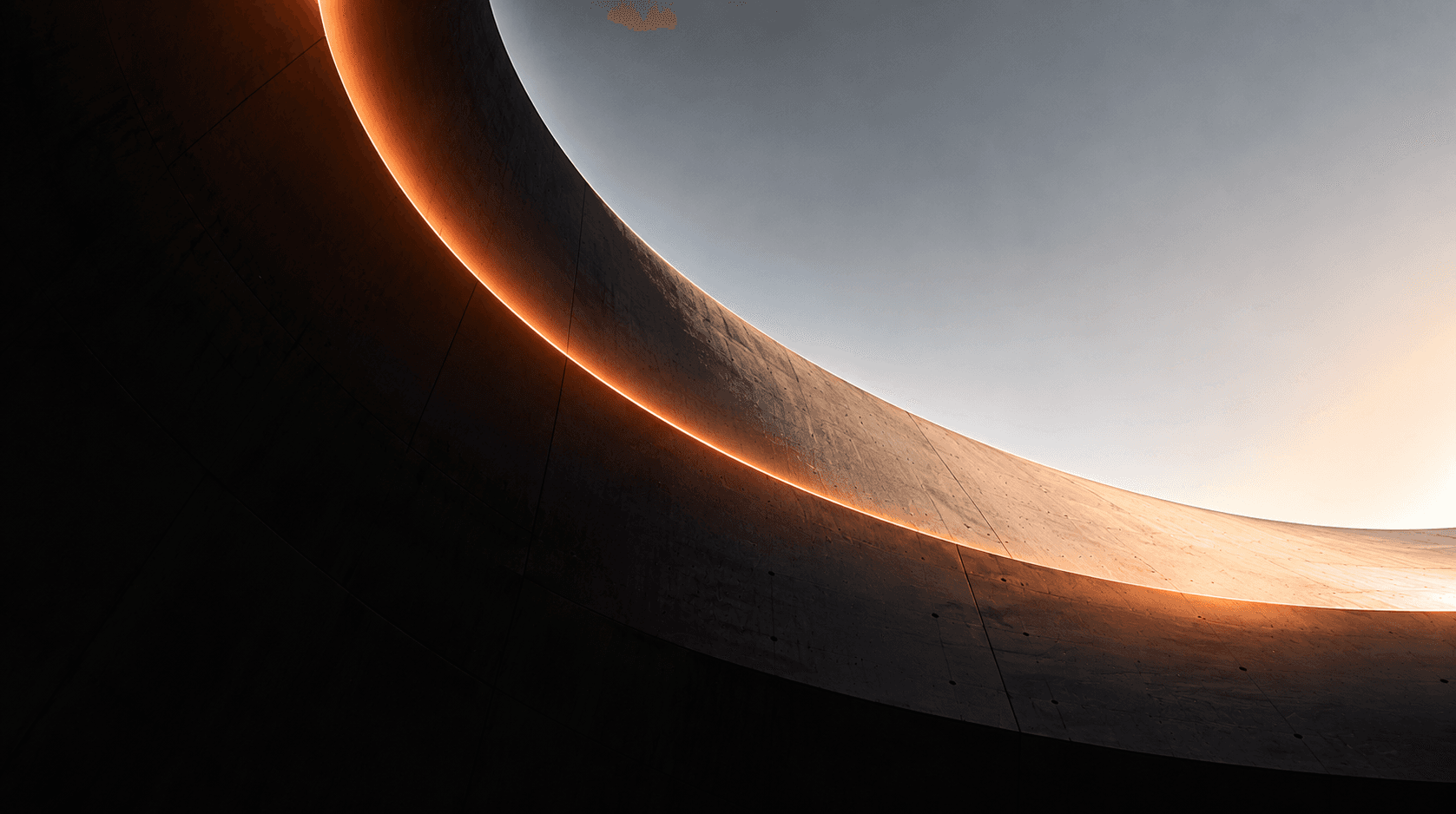 Curved concrete architecture edged with a thin orange glow against a pale sky